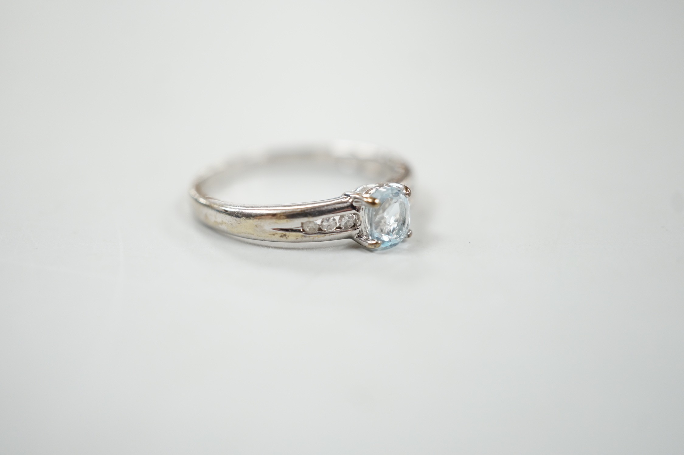 A modern 9ct white gold and oval cut blue topaz ring, with diamond chip set shoulders, size N, gross weight 2 grams.